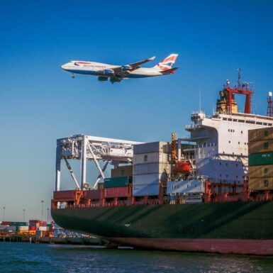 A plane comes in to land over a container ship at a port